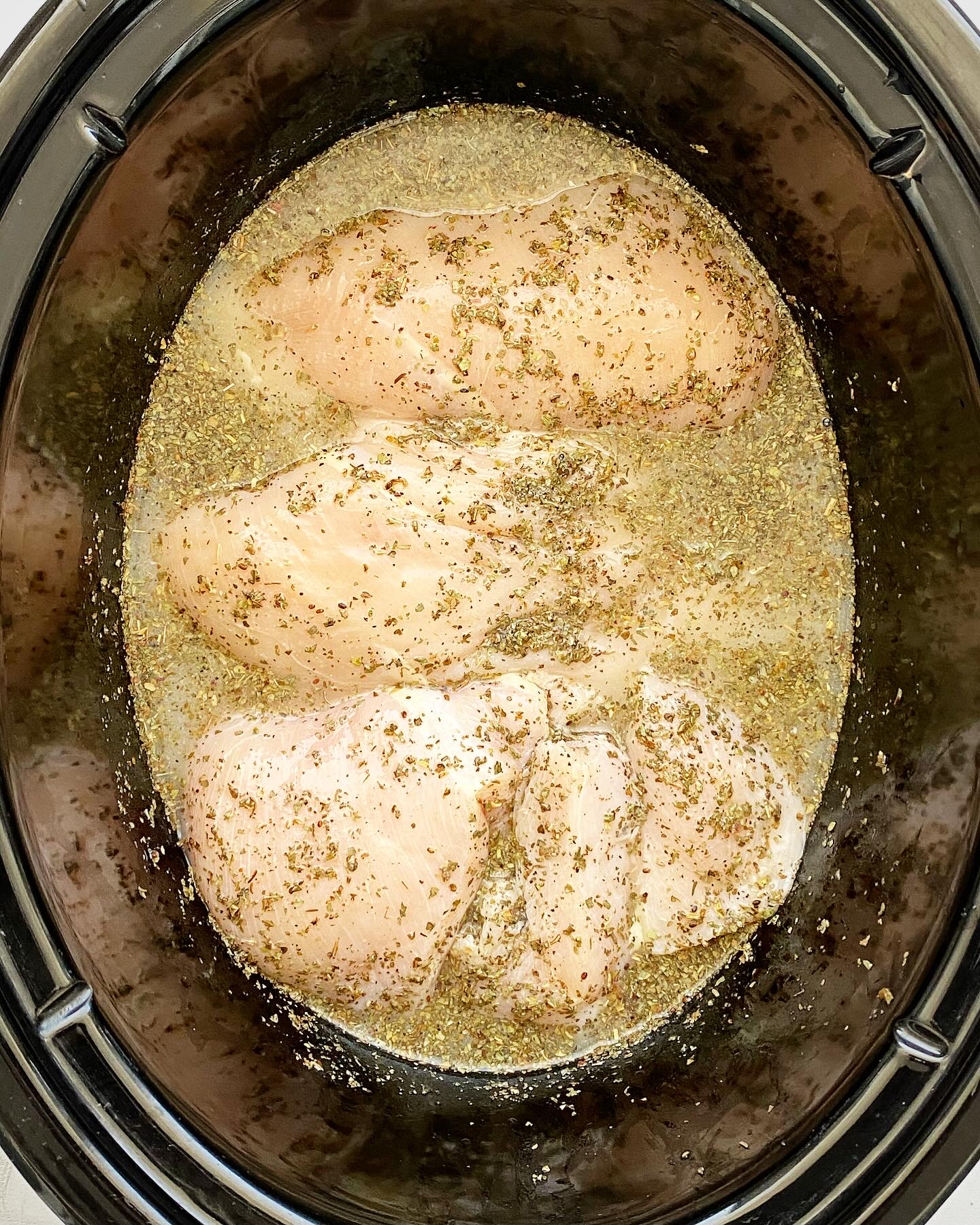 overhead shot of uncooked creamy lemon basil chicken in a black slow cooker