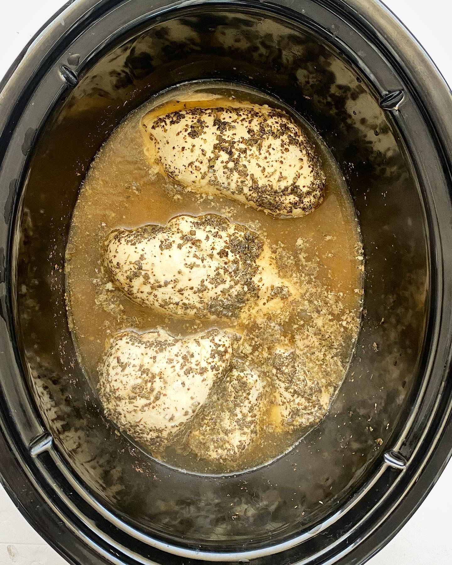 overhead shot of cooked creamy lemon basil chicken in a black slow cooker