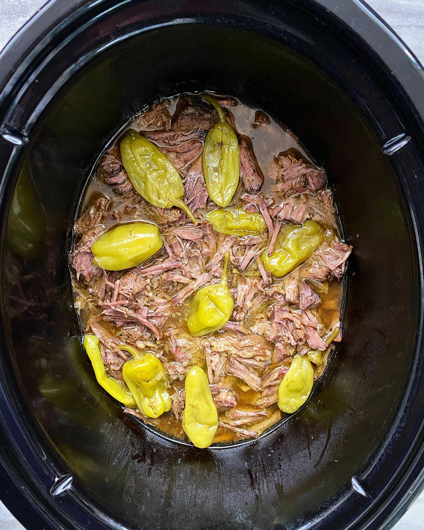 overhead shot of cooked and shredded Mississippi roast in a black slow cooker