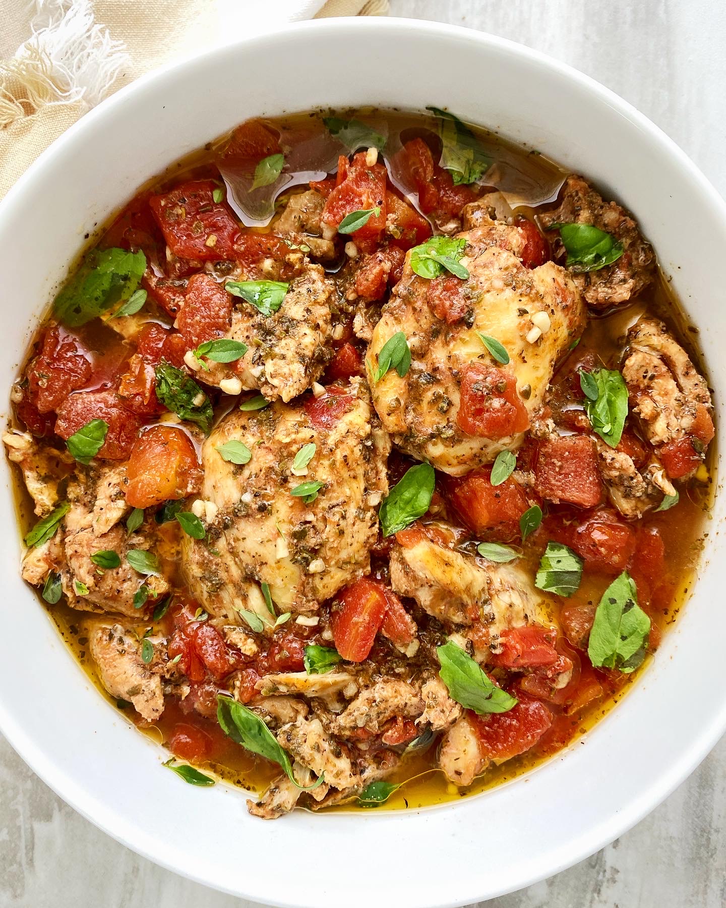 overhead shot of cooked tomato garlic chicken & herbs in a white bowl