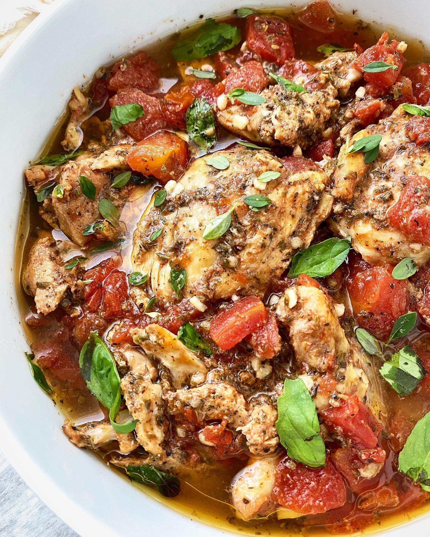 side view shot of cooked tomato garlic chicken & herbs in a white bowl