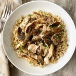 overhead shot of shredded, herb chicken on top of cooked brown rice with a silver fork on the top left