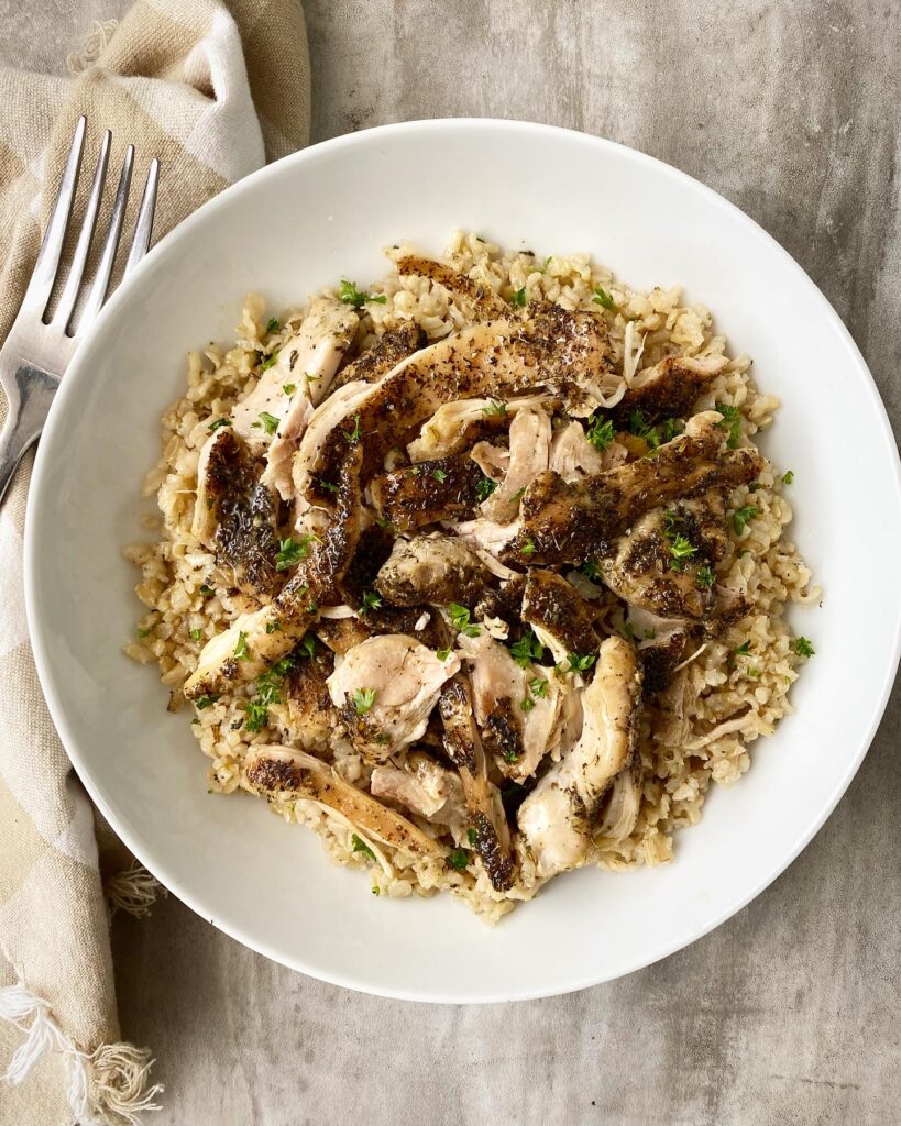 overhead shot of shredded, herb chicken on top of cooked brown rice with a silver fork on the top left