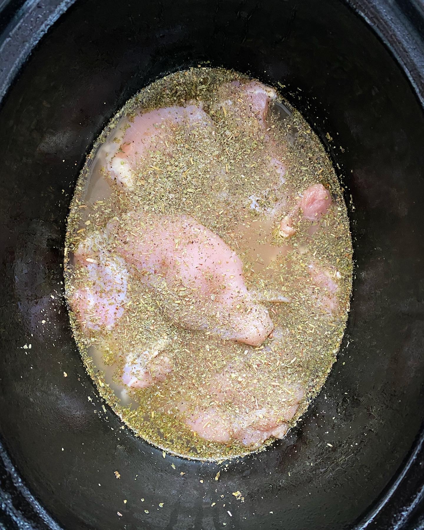 overhead shot of uncooked chicken & rice in a black crockpot