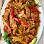 overhead shot of slow cooker chicken fajitas on a white plate garnished with cilantro, avocado, and limes