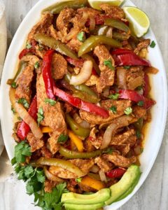 overhead shot of slow cooker chicken fajitas on a white plate garnished with cilantro, avocado, and limes