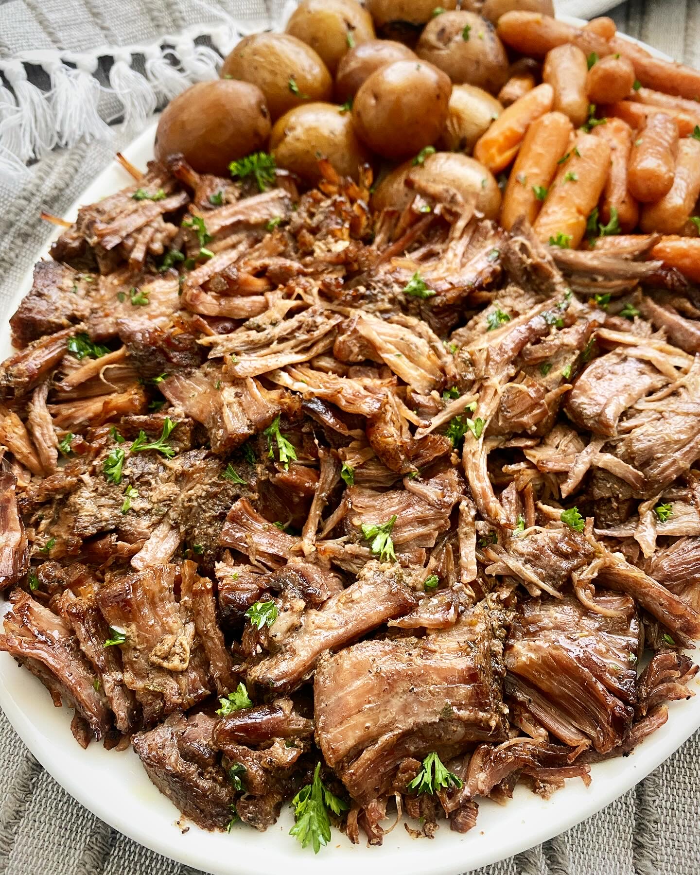 close up shot of cooked beef roast on a white platter with potatoes and carrots