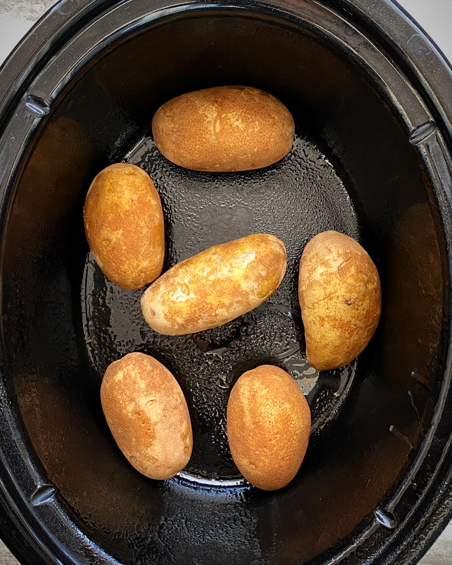overhead shot of 6 russet potatoes in a black slow cooker