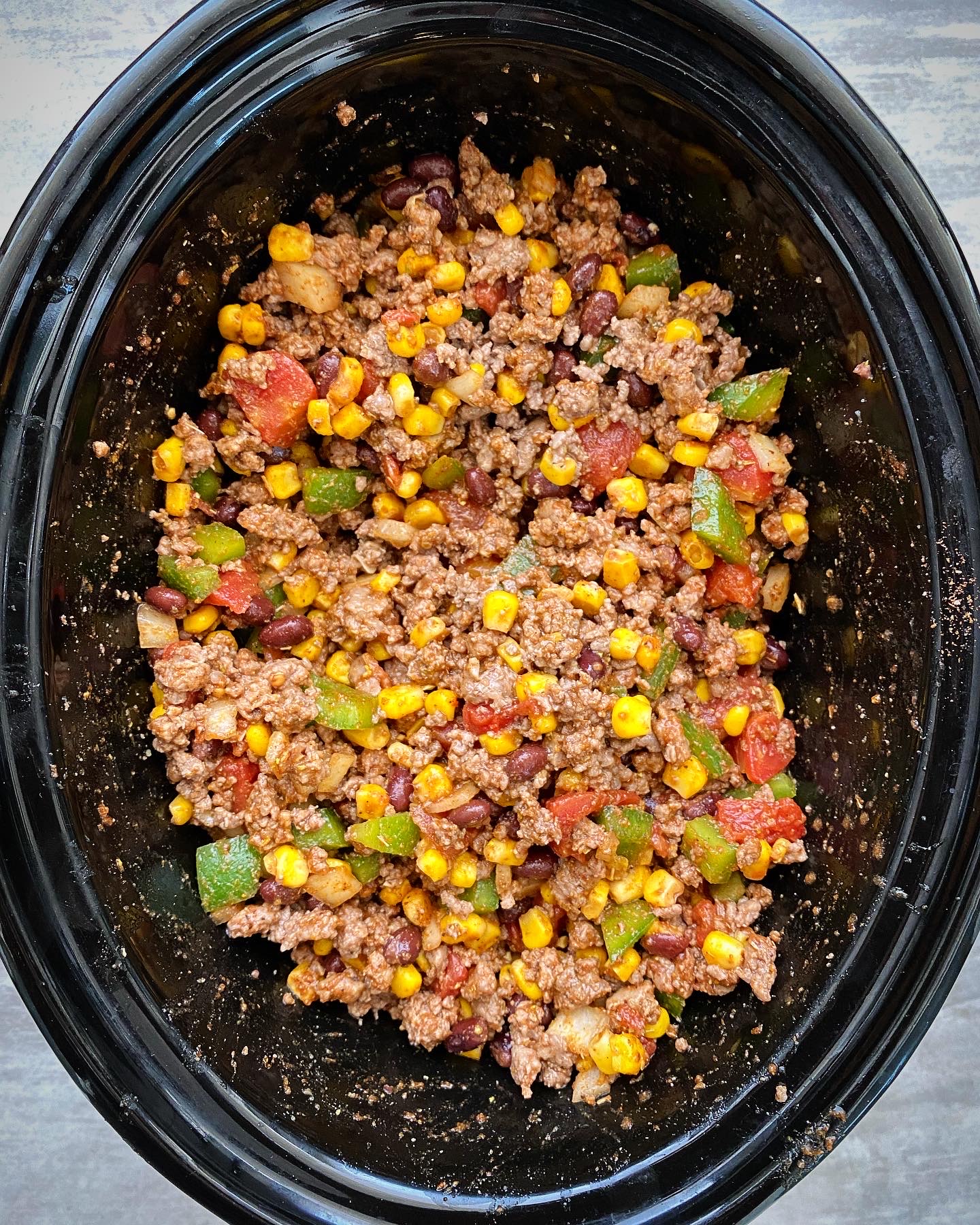 overhead shot of uncooked crockpot Tex-Mex ground meat in a black slow cooker