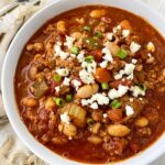 overhead shot of Cooker Buffalo Chicken Chili in a white bowl garnished with blue cheese and green onion