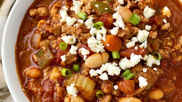 overhead shot of Cooker Buffalo Chicken Chili in a white bowl garnished with blue cheese and green onion
