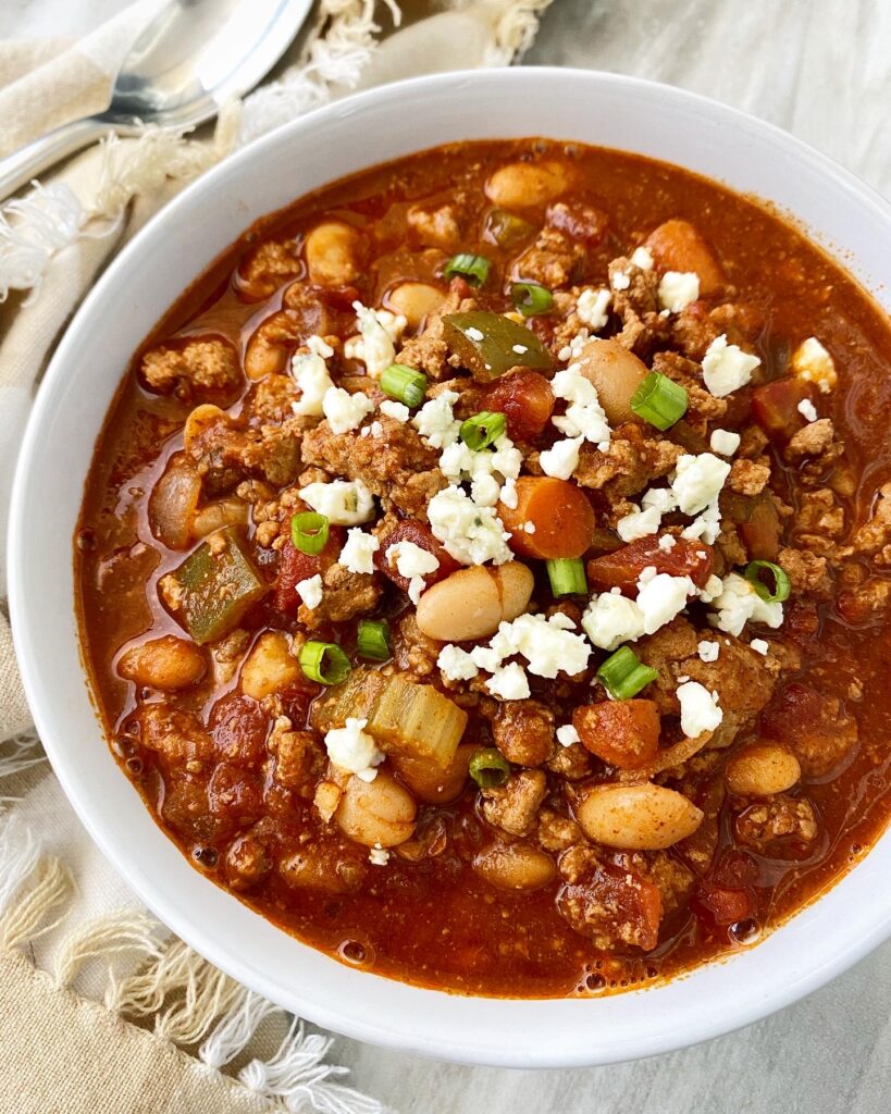 overhead shot of Cooker Buffalo Chicken Chili in a white bowl garnished with blue cheese and green onion
