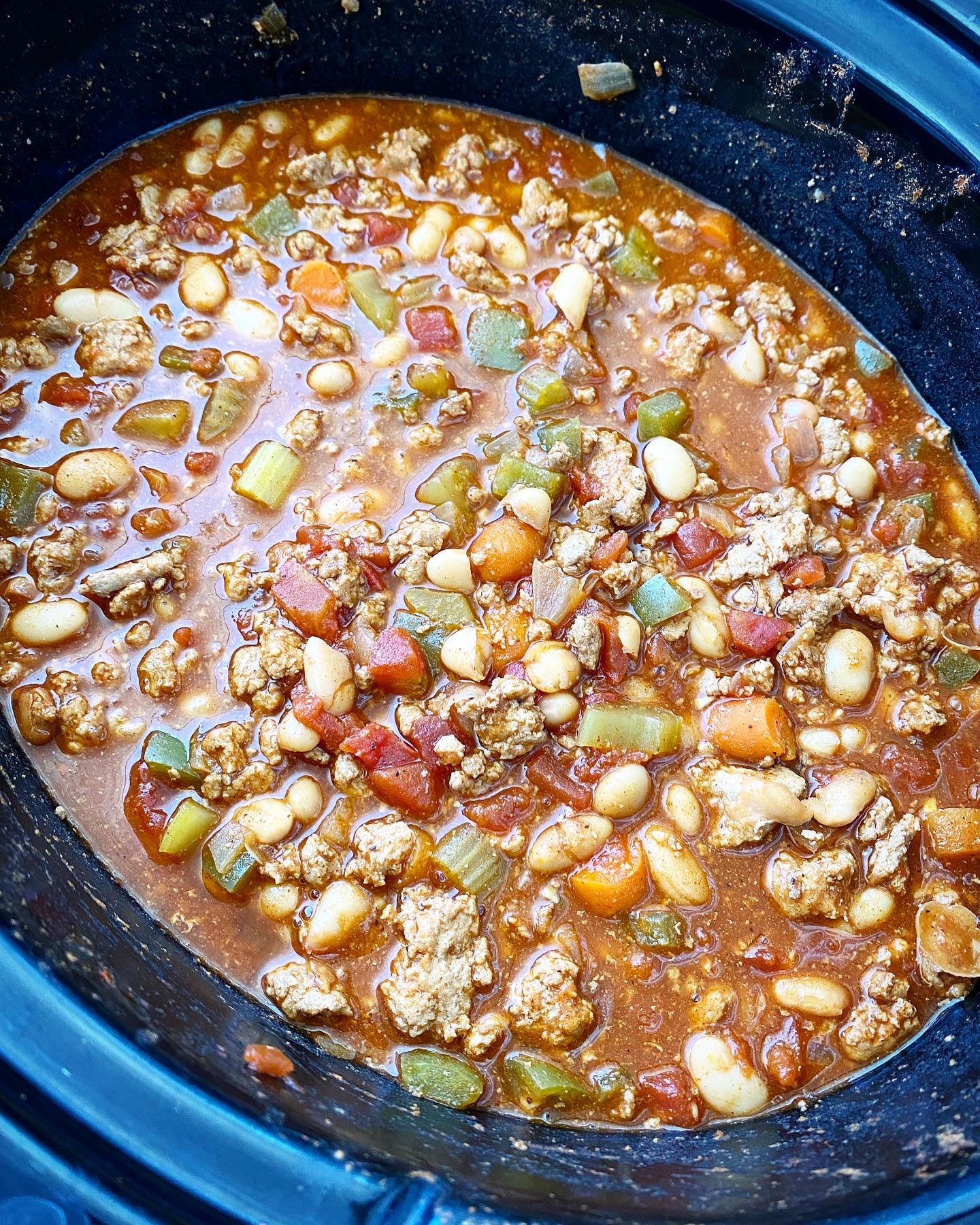 overhead side shot of cooked buffalo chicken chili in a black slow cooker