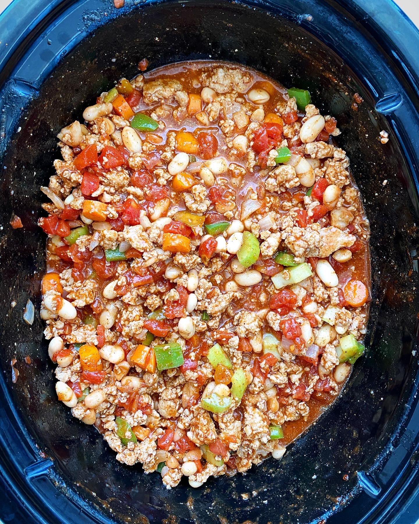 overhead shot of raw buffalo chicken chili in a black slow cooker
