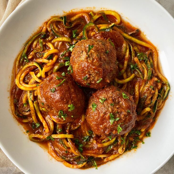 overhead shot of 3 large meatballs over zucchini noodles in a white bowl