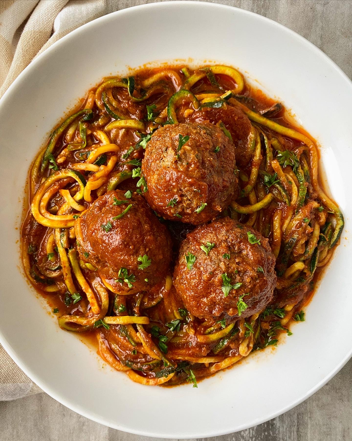 overhead shot of 3 large meatballs over zucchini noodles in a white bowl
