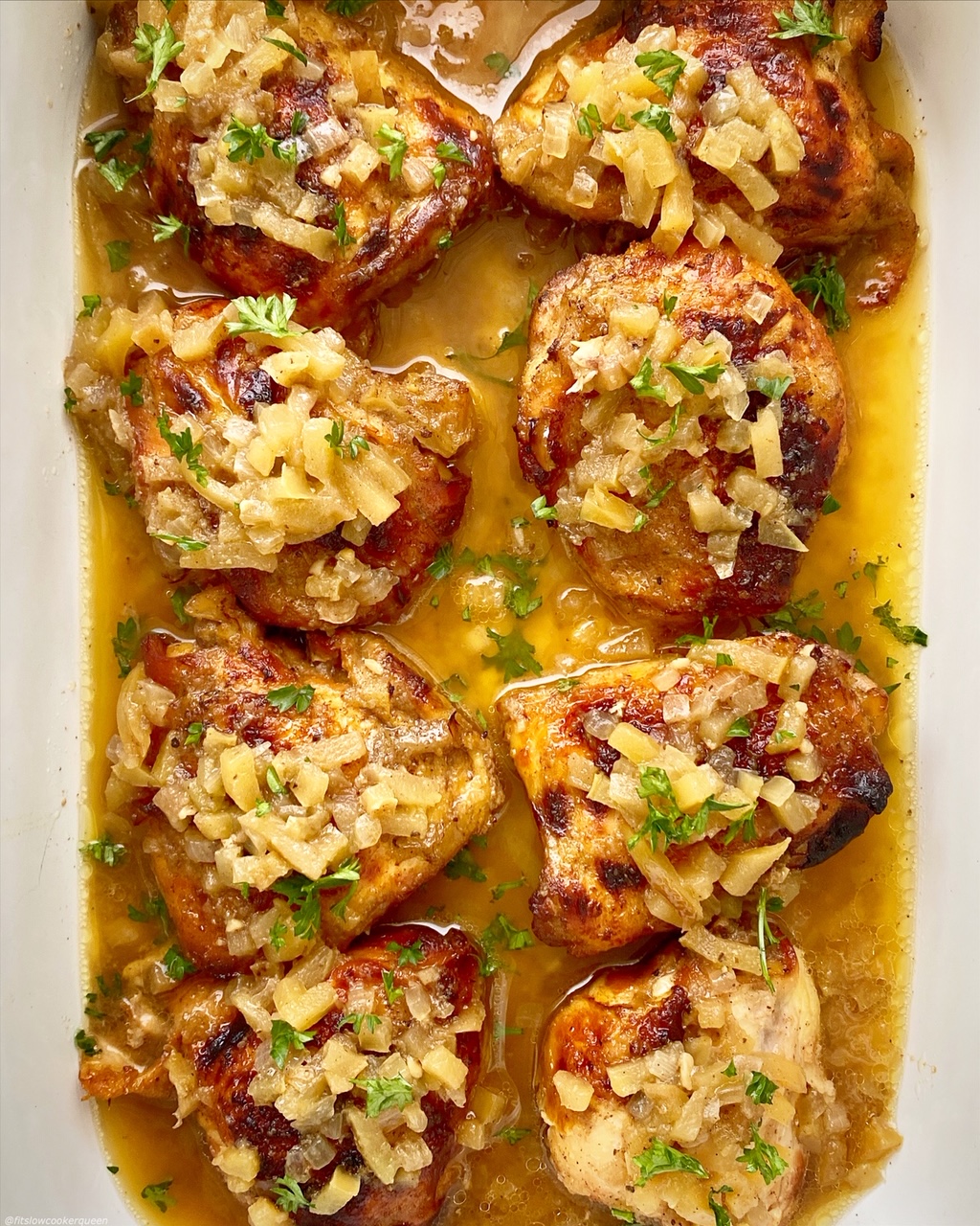 overhead shot of cooked chicken with apples and honey in a white baking dish