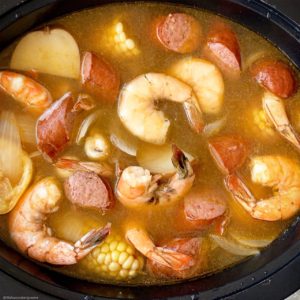 overhead shot of adding cooked seafood boil in a black slow cooker