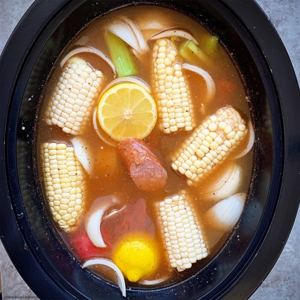overhead shot of adding uncooked seafood boil in a black slow cooker