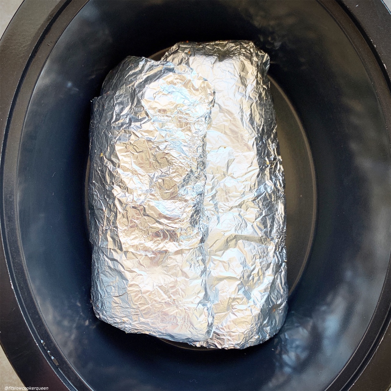 overhead shot of pork ribs wrapped in foil in the slow cooker