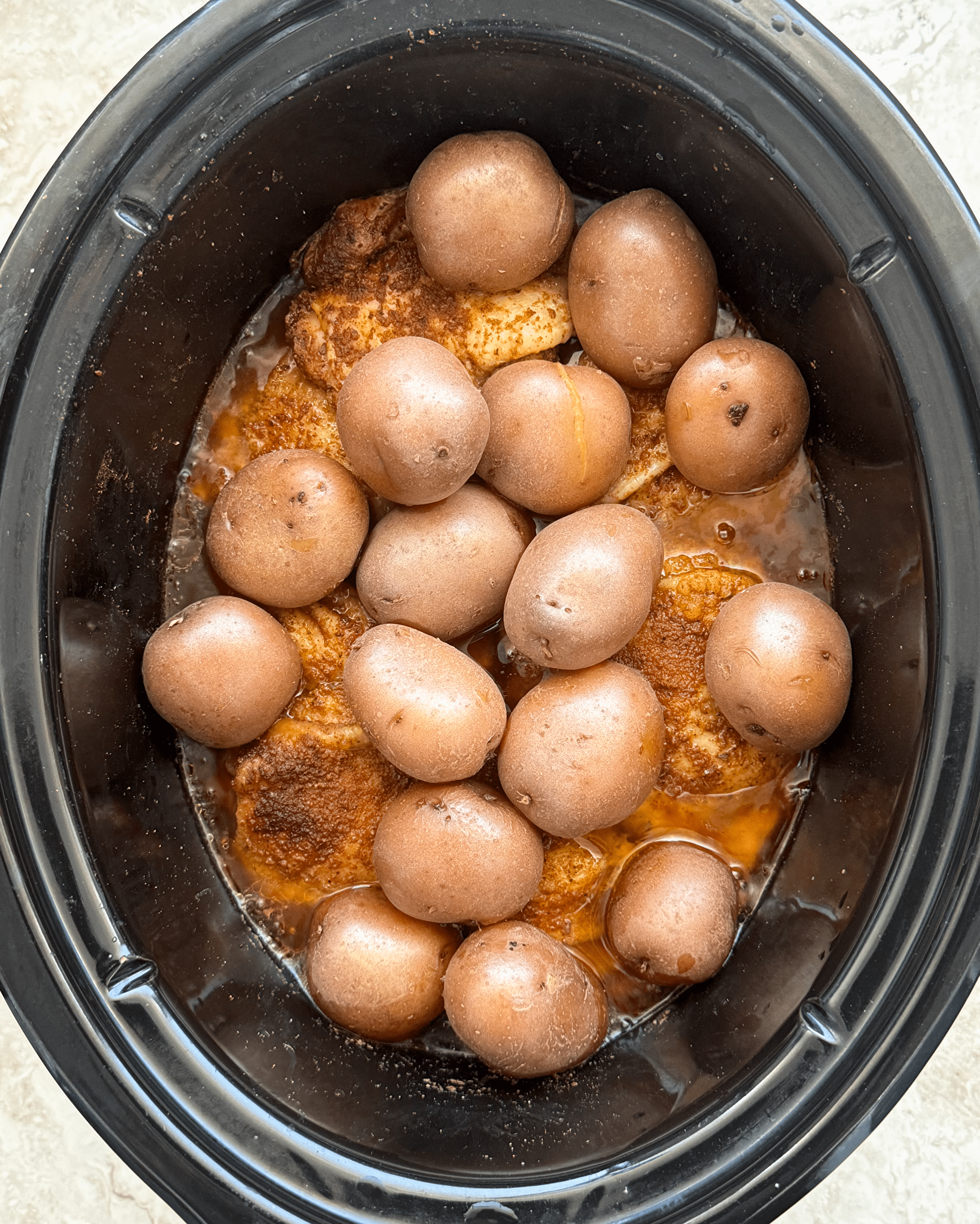 overhead shot of cooked chicken thigh and potatoes in a black slow cooker