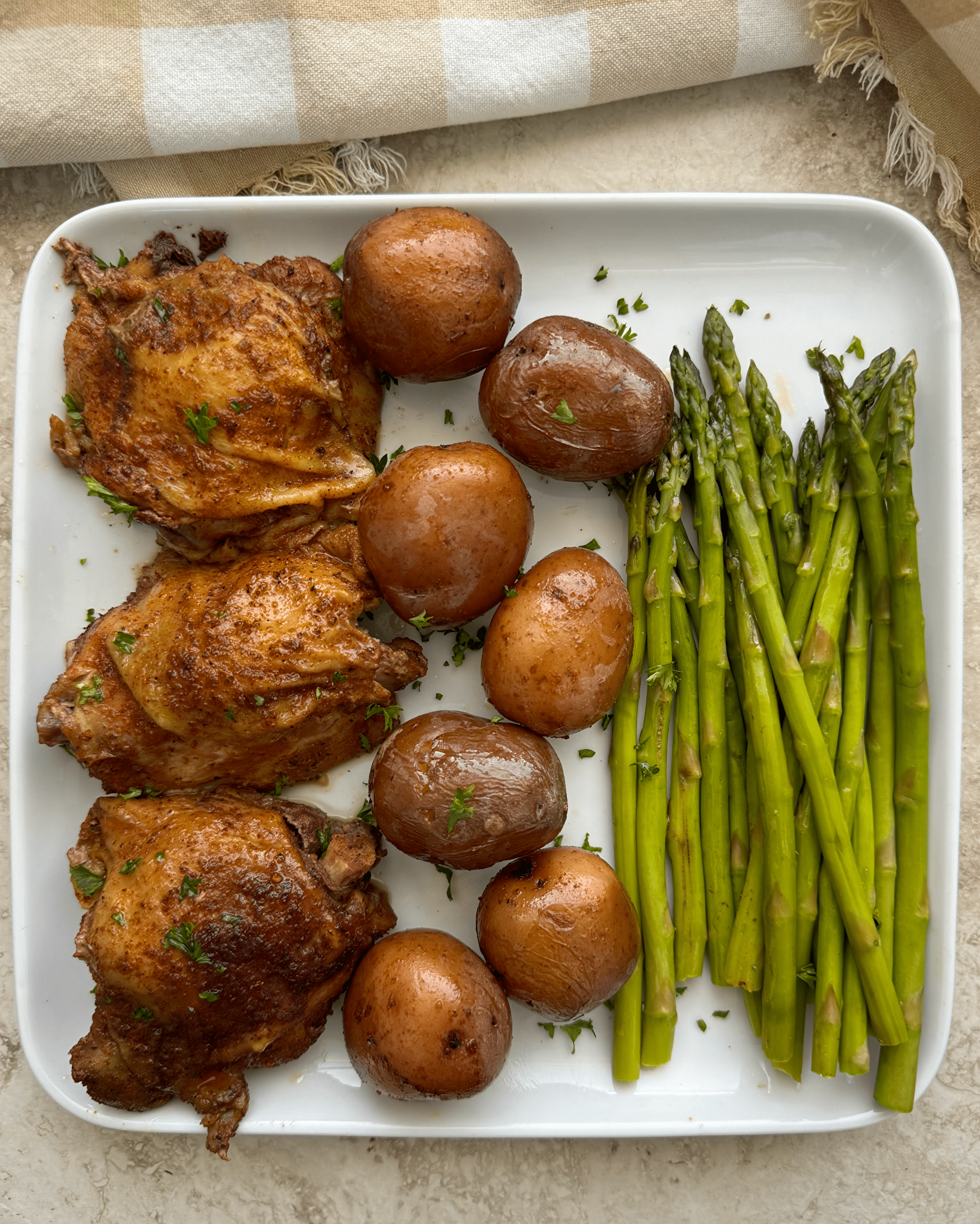 over head shot of 3 chicken thighs, 7 baby red potatoes, and asparagus on a white plate