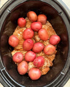 overhead shot of uncooked chicken thigh and potatoes in a black slow cooker