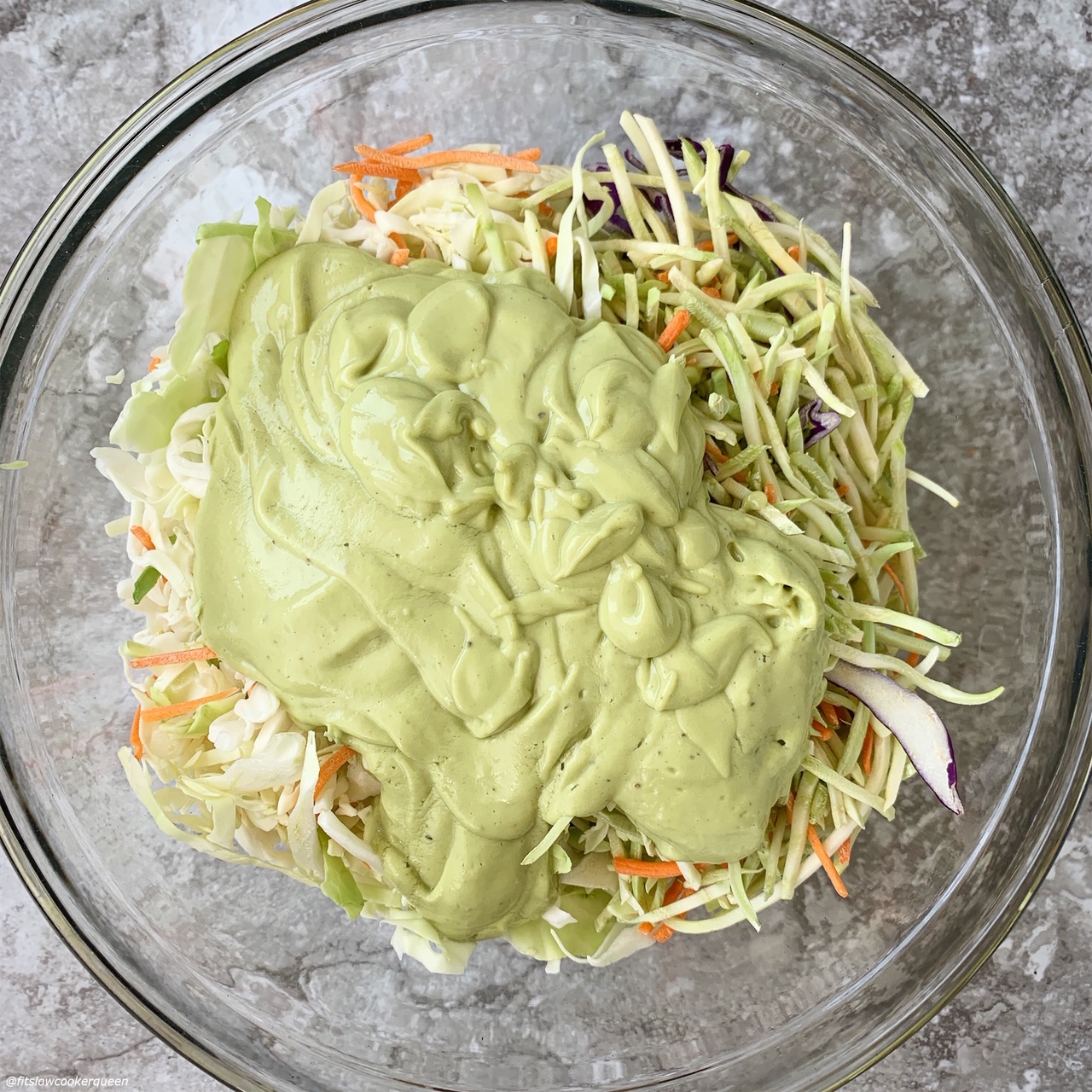 bowl of broccoli slaw & coleslaw with avocado sauce on top before it's mixed