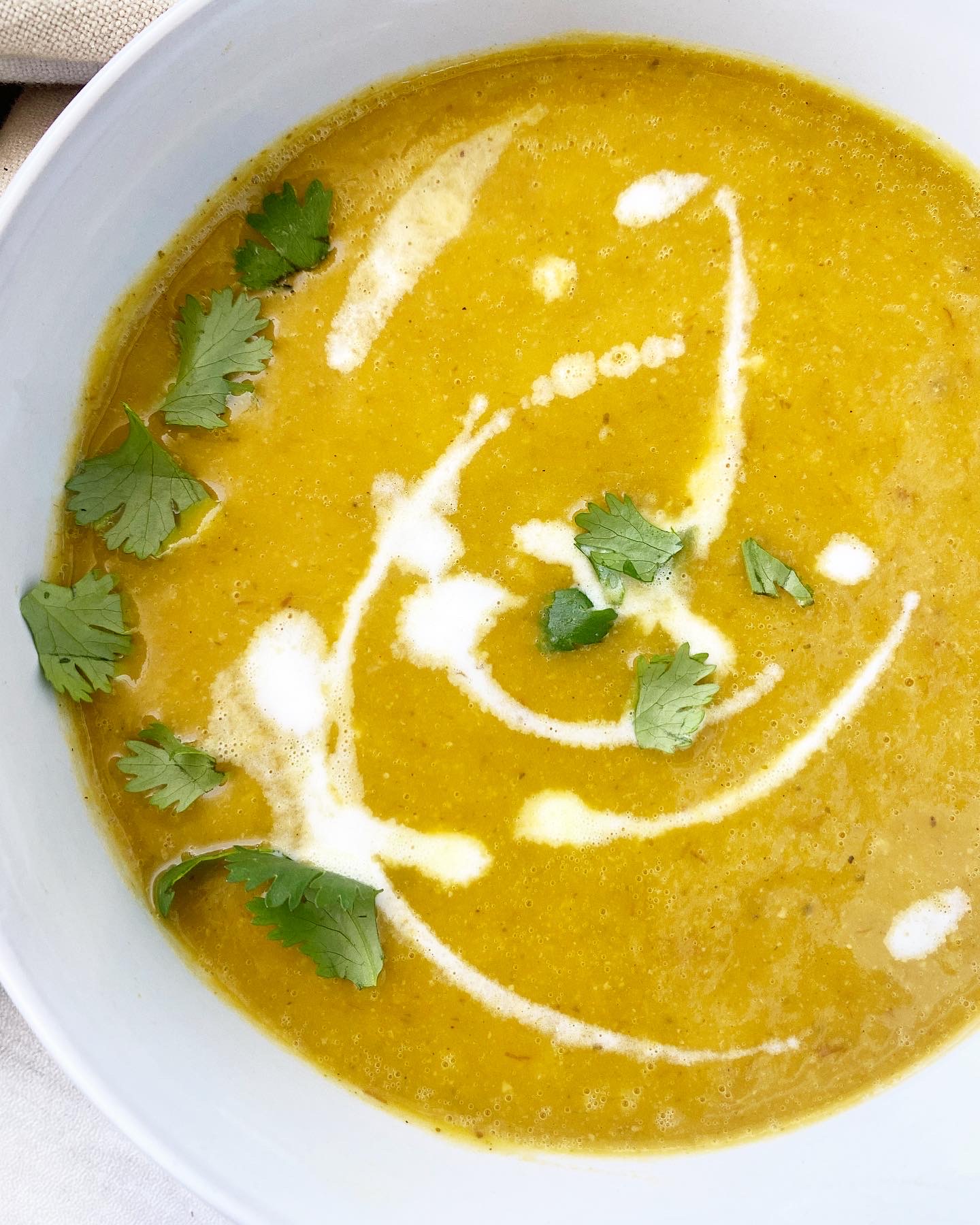 overhead side view shot of cooked butternut squash soup in a white bowl garnished with coconut milk, cilantro,