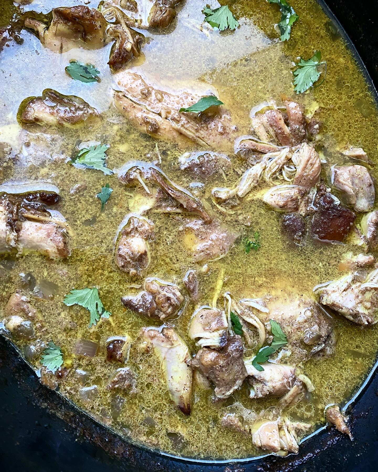 overhead shot of cooked Caribbean chicken in a black slow cooker garnished with fresh cilantro