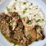 overhead shot of Caribbean chicken in a white bowl next to white rice garnished with fresh cilantro