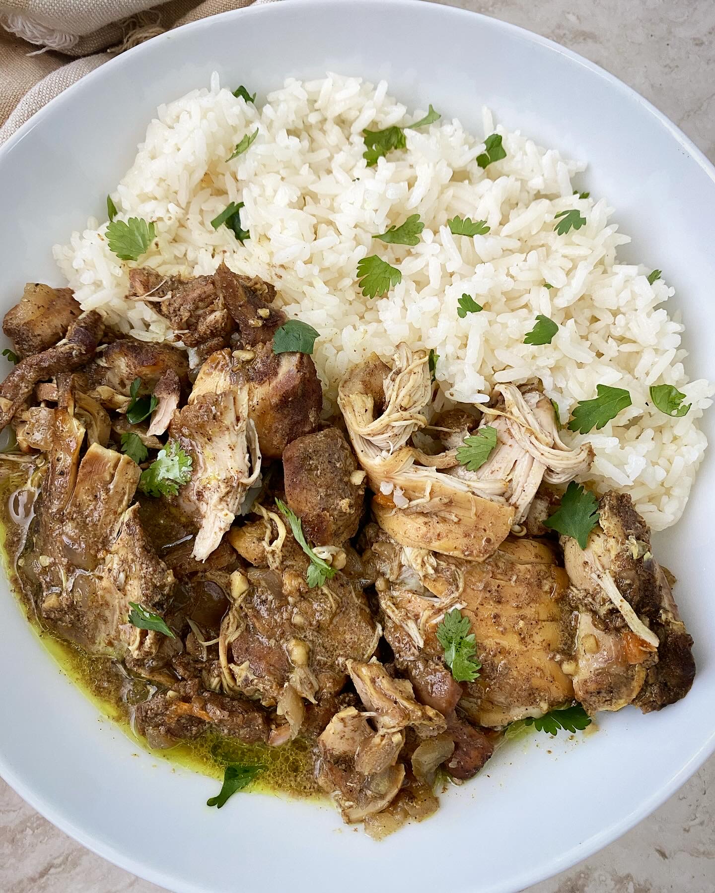 overhead shot of Caribbean chicken in a white bowl next to white rice garnished with fresh cilantro