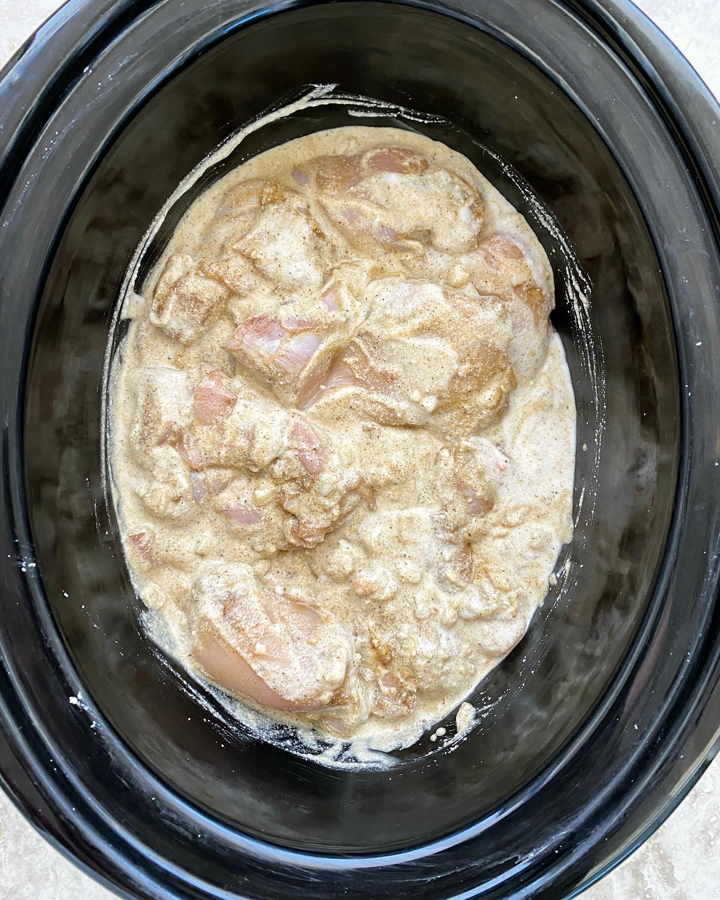 overhead shot of uncooked Caribbean chicken in a black slow cooker