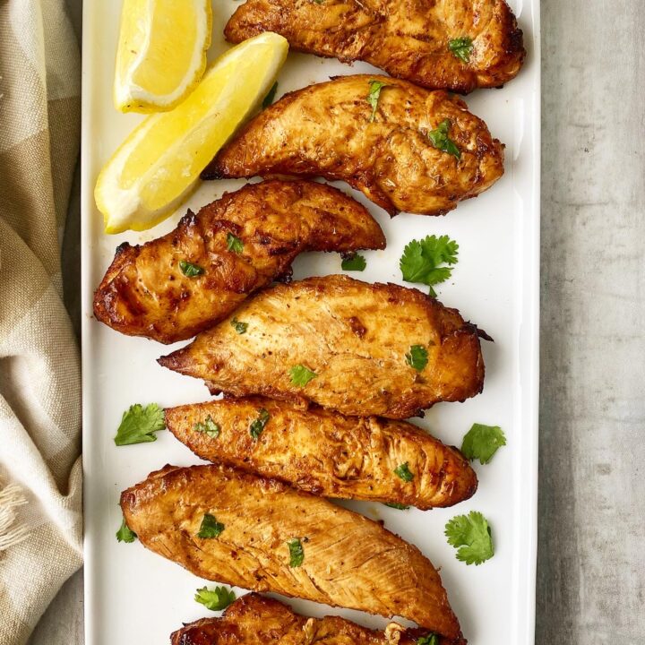 spicy naked chicken tenders topped with green cilantro on a white plate with lemon wedges