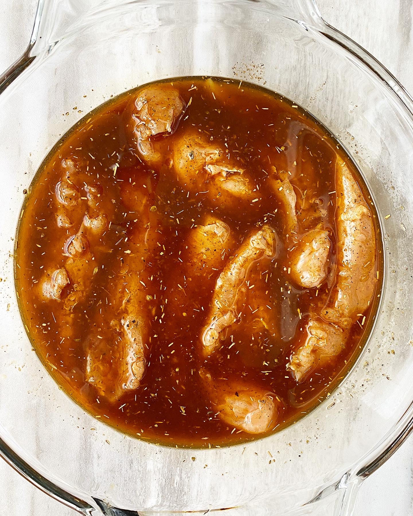chicken tenders with marinade on top in a clear bowl