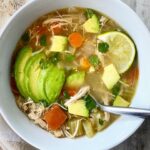 overhead shot of chicken avocado soup in a white bowl with a spoon