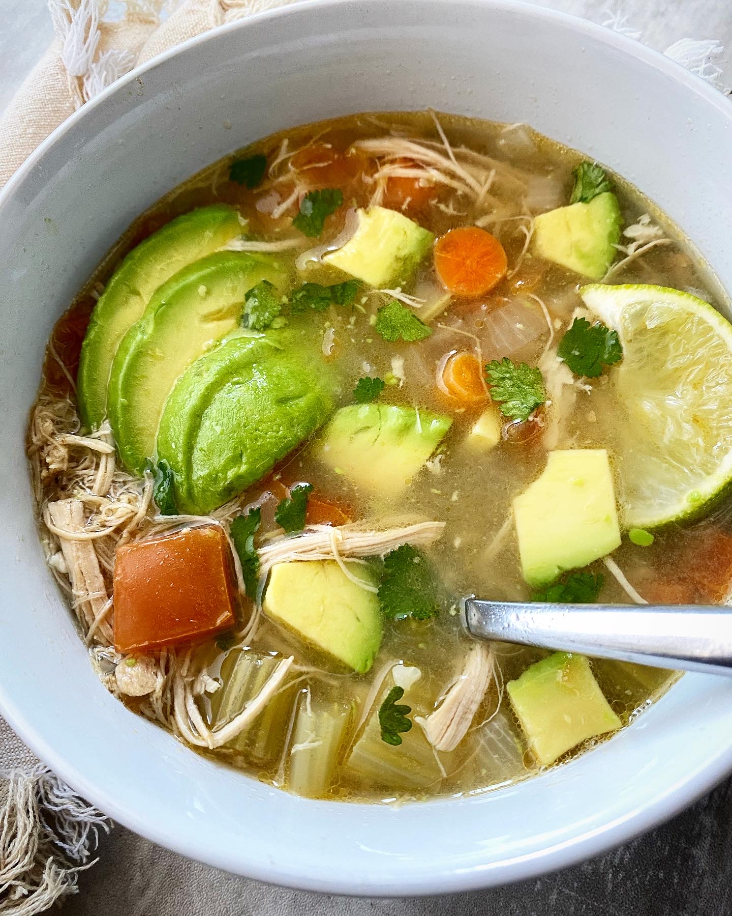 close up shot of chicken avocado soup in a white bowl with a spoon