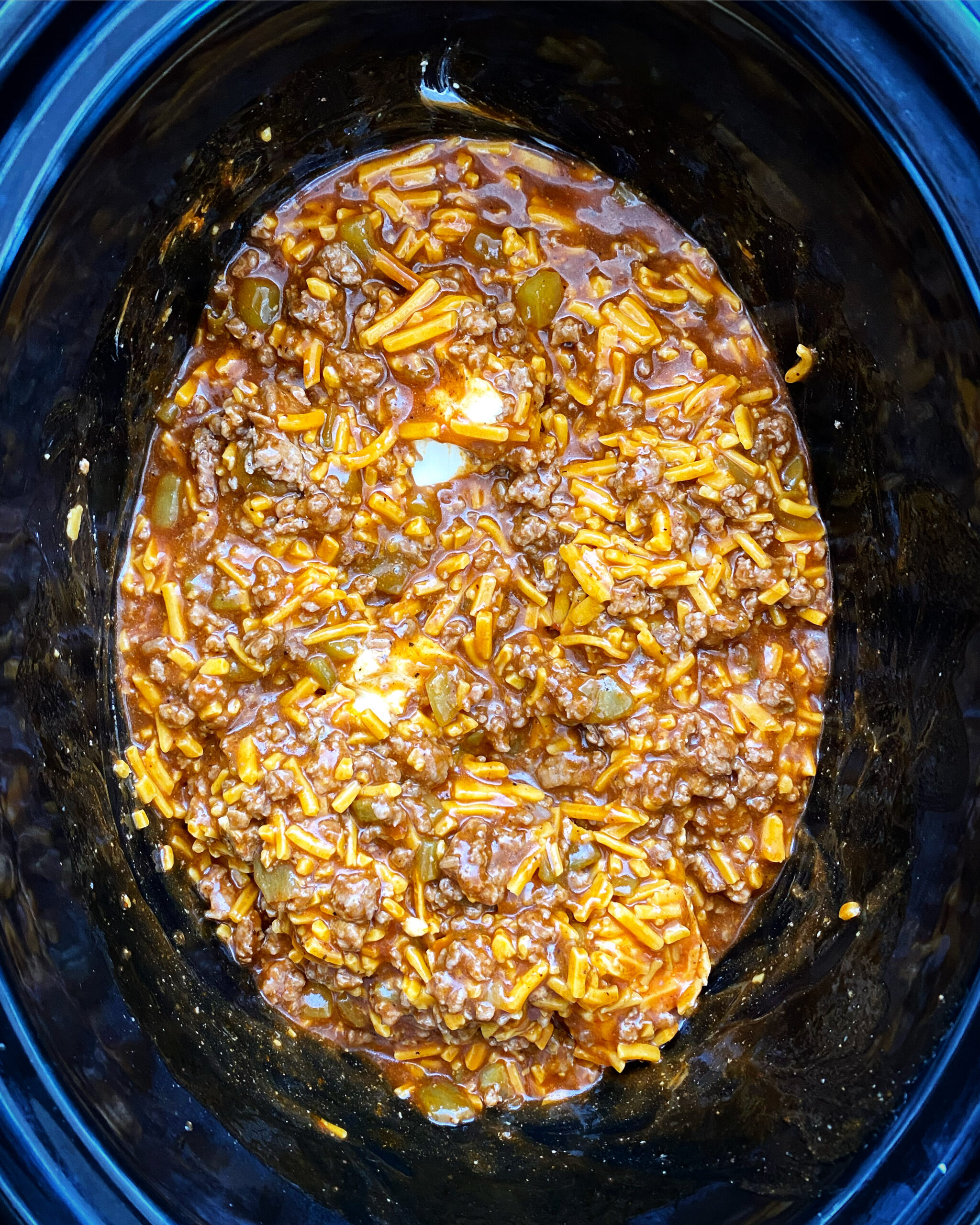 overhead shot of uncooked enchilada dip in a black slow cooker