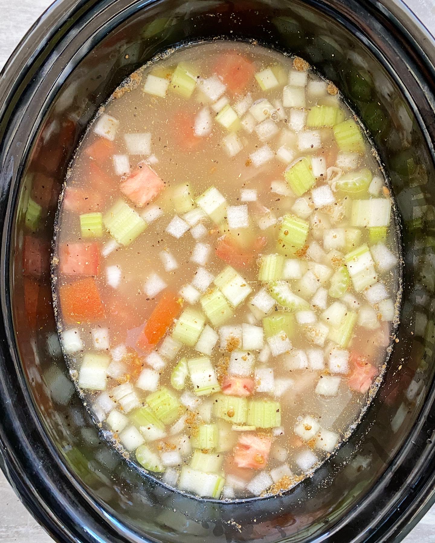 overhead shot of cooked chicken soup in a black slow cooker