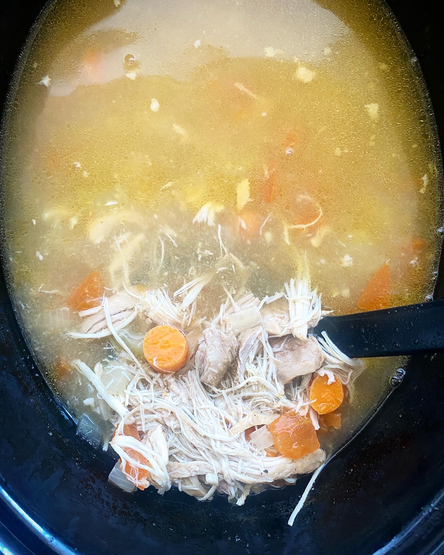 overhead shot of cooked chicken soup in a black slow cooker