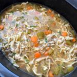 close up shot of cooked chicken noodle soup in a black slow cooker