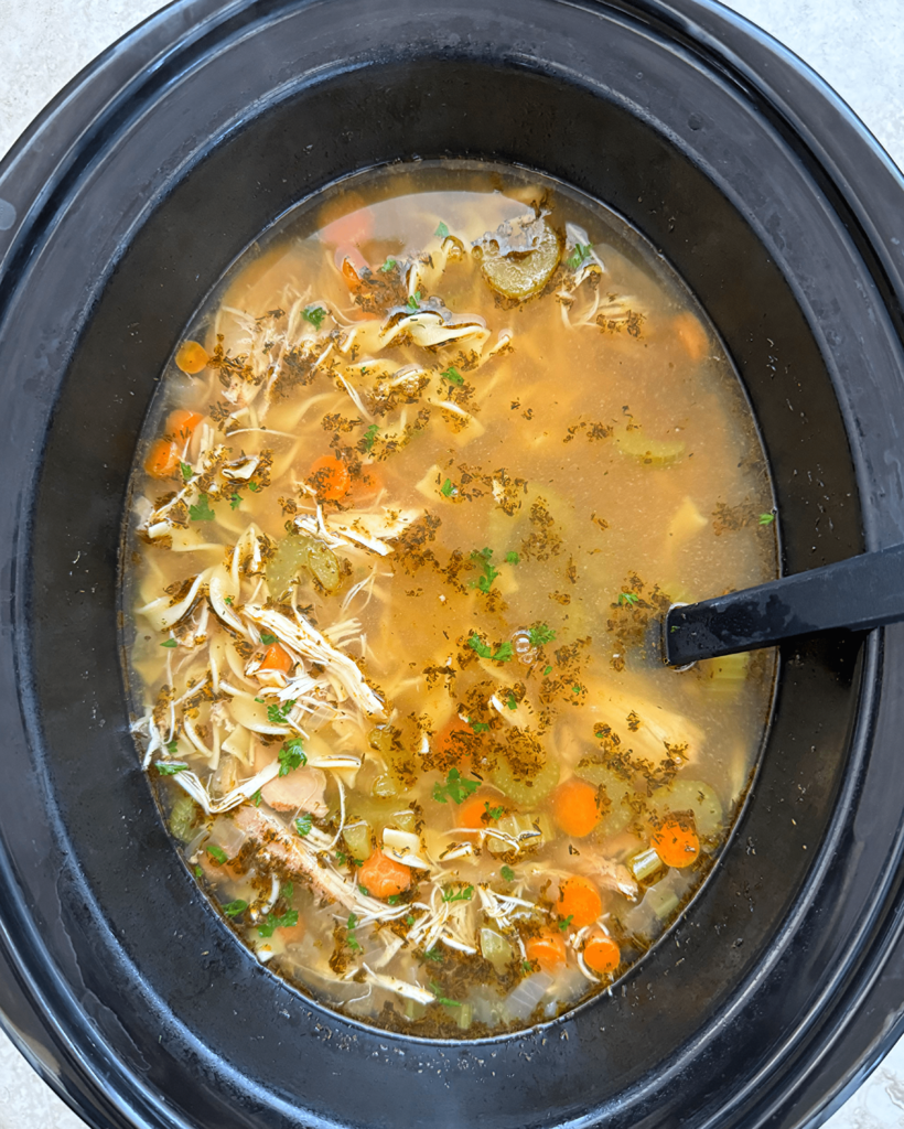 overhead shot of cooked chicken noodle soup in a black slow cooker