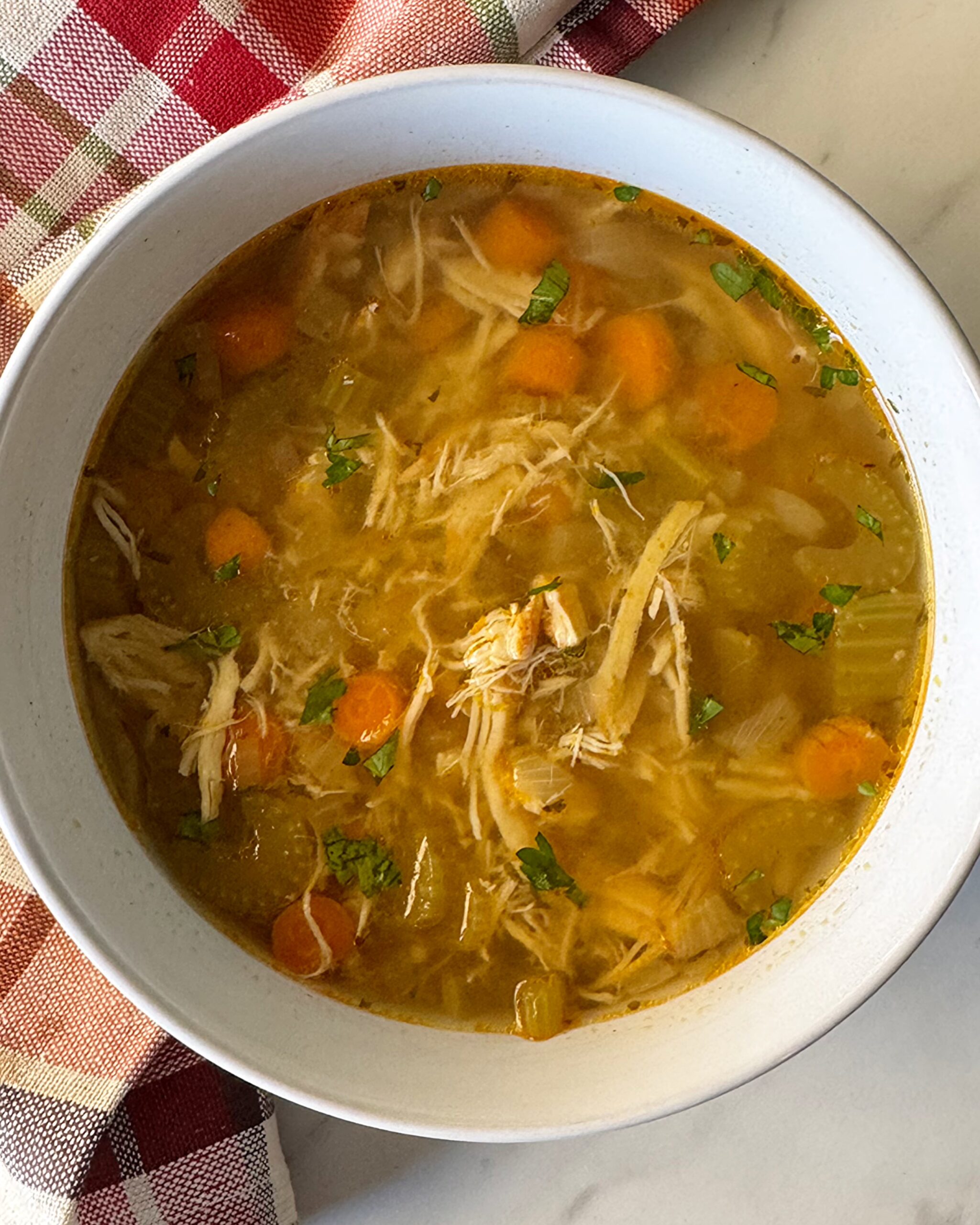 overhead shot of cooked chicken soup in a white bowl