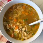 overhead shot of cooked chicken soup in a white bowl with a silver spoon