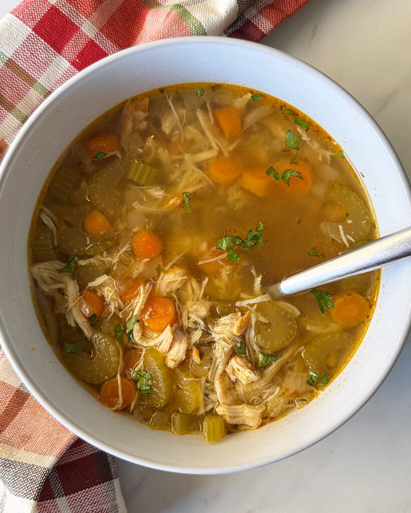 overhead shot of cooked chicken soup in a white bowl with a silver spoon