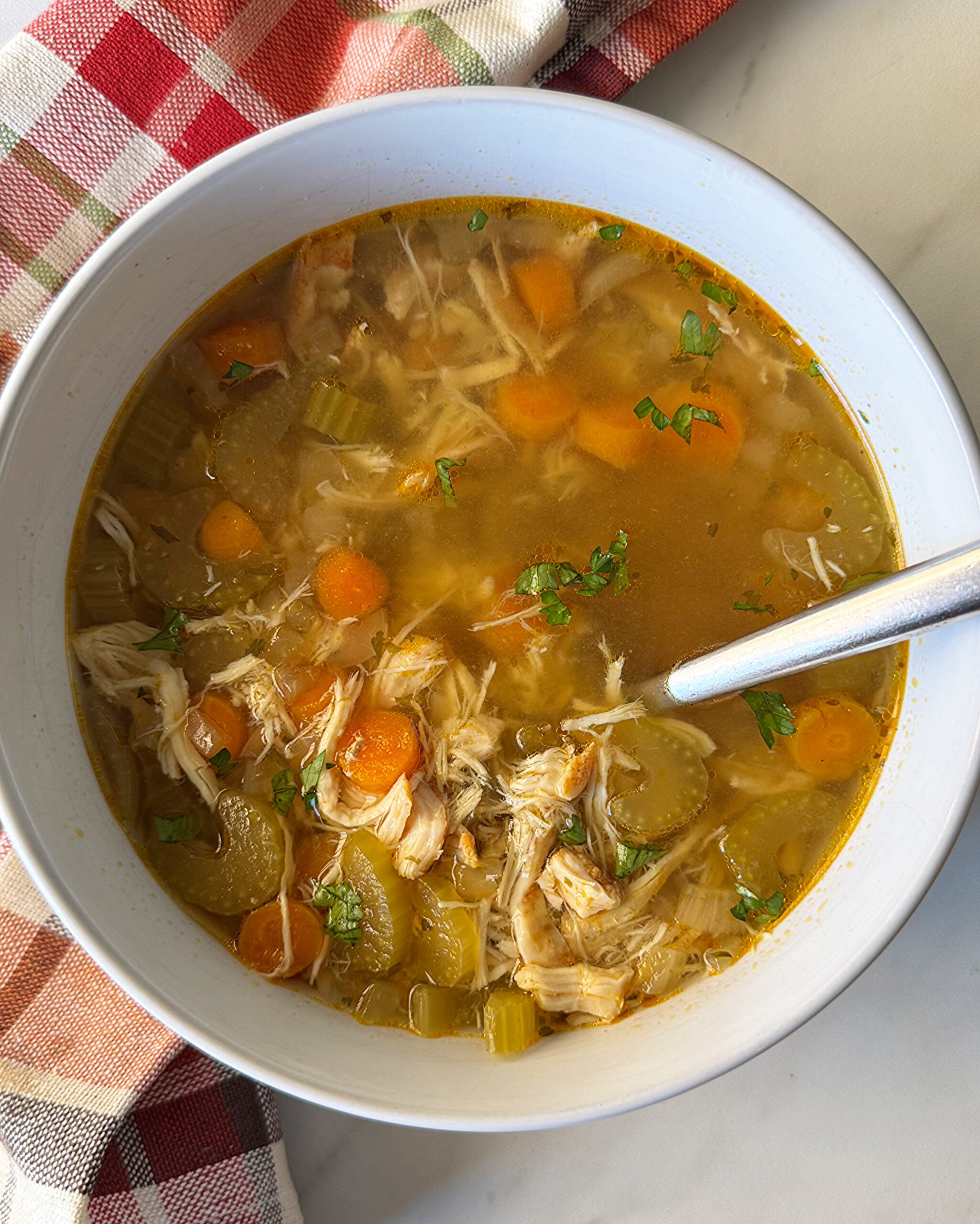 overhead shot of cooked chicken soup in a white bowl with a silver spoon