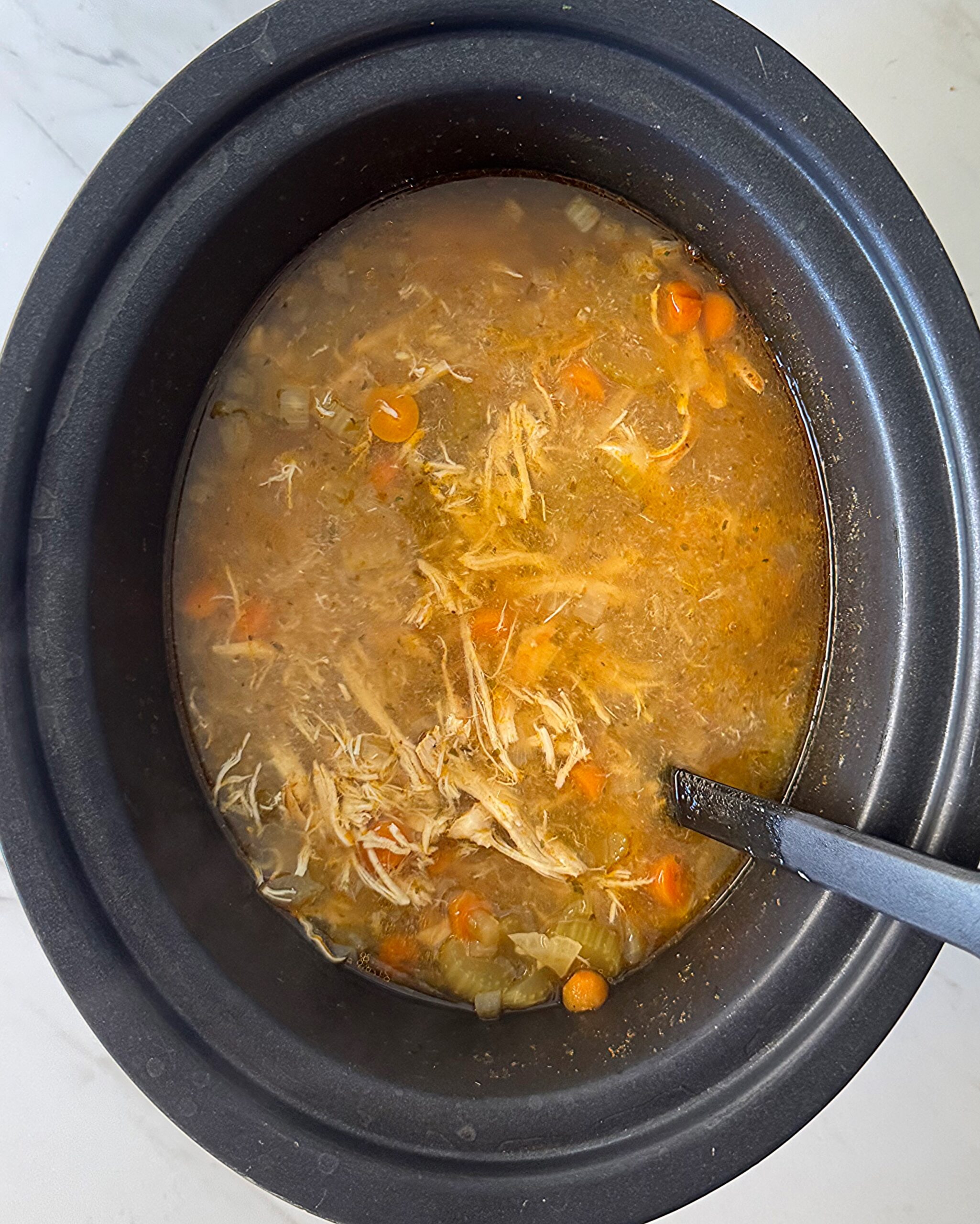 ove3rhead shot of cooked chicken soup in a black slow cooker