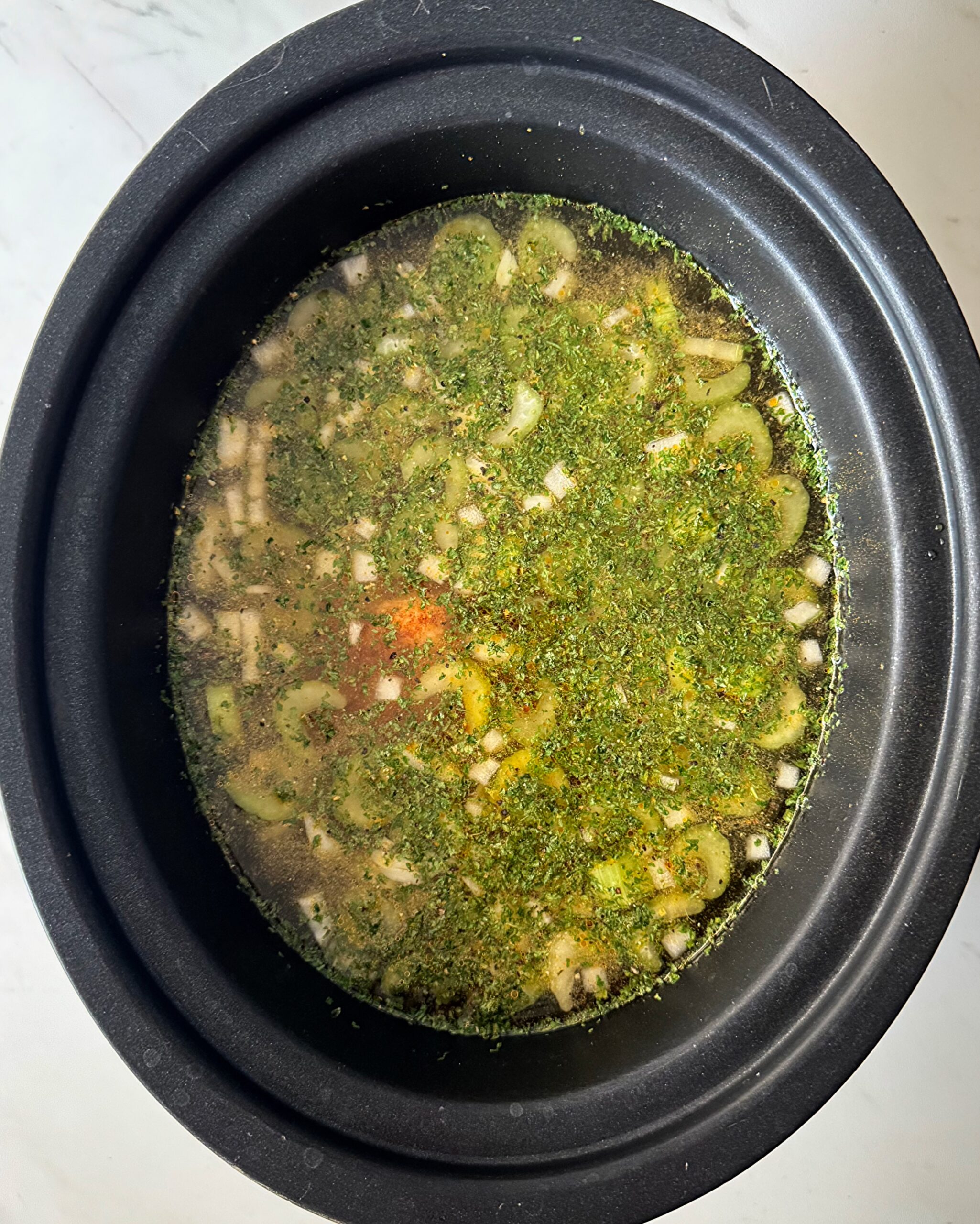 ove3rhead shot of uncooked chicken soup in a black slow cooker
