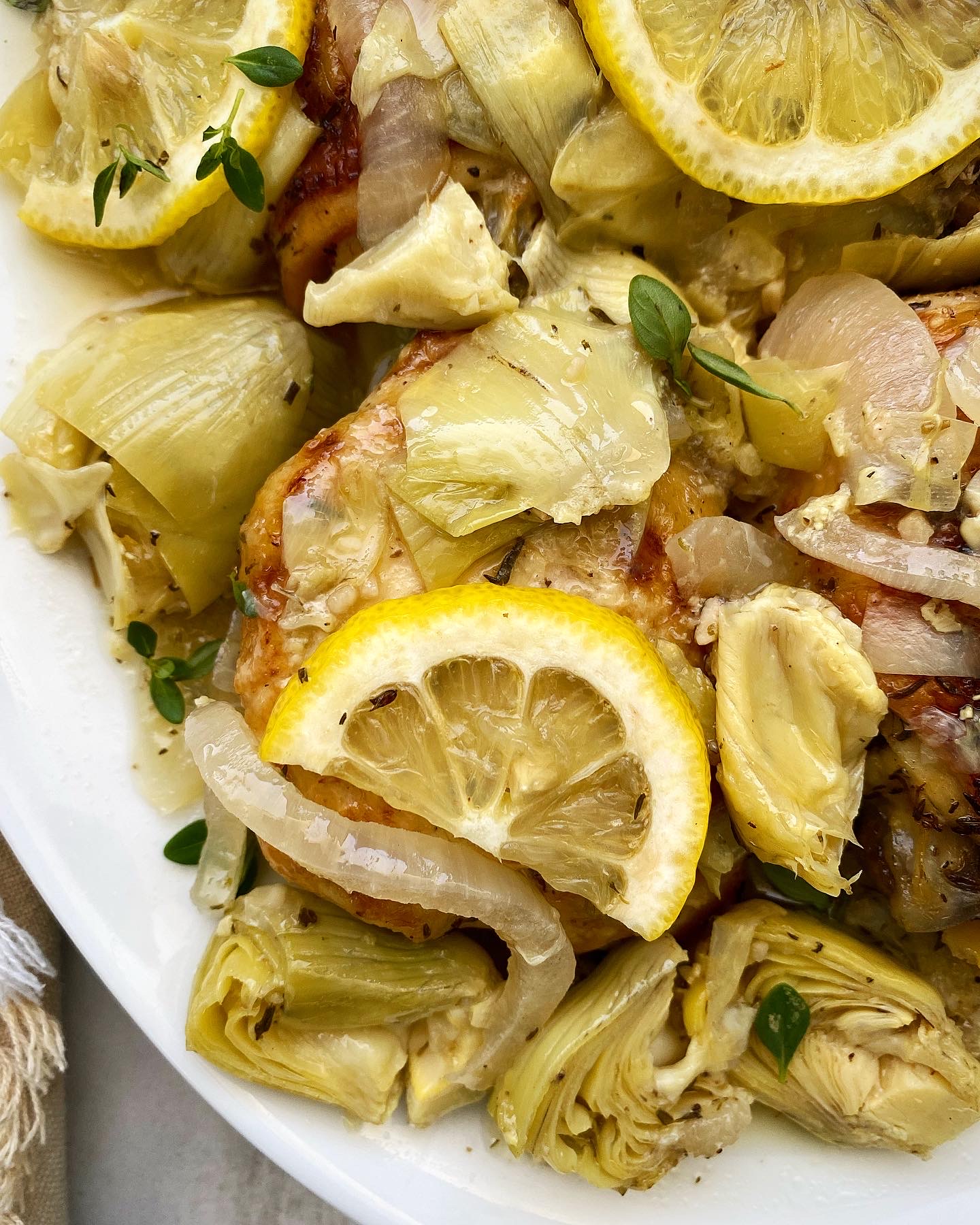 close up of lemon artichoke chicken on a white plate with lemon slices and fresh thyme
