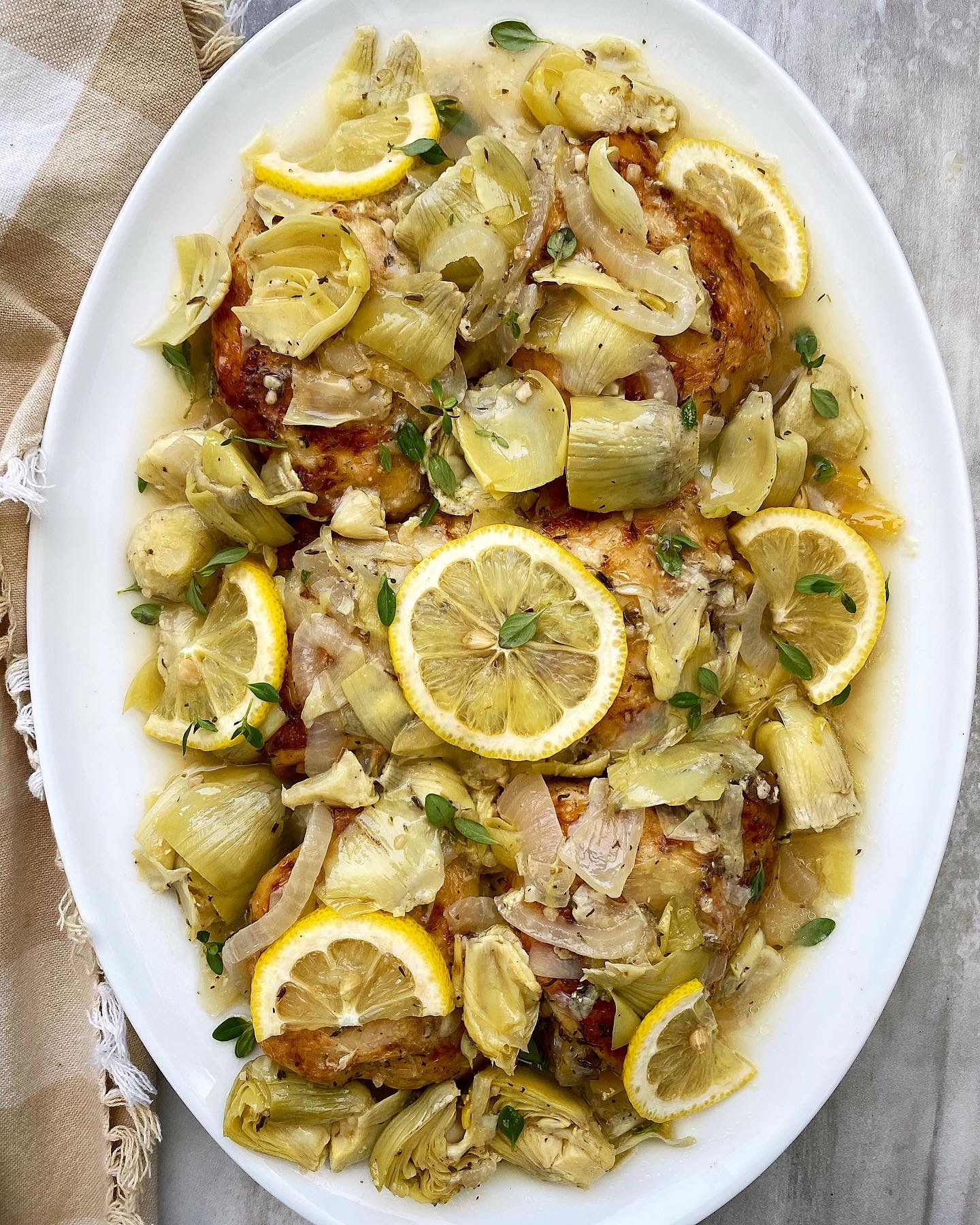 overhead shot of lemon artichoke chicken on a white plate with lemon slices and fresh thyme